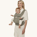 A woman wearing the Ergobaby Omni Deluxe Mesh baby carrier in Soft Olive, with a little baby being carried facing outwards. 