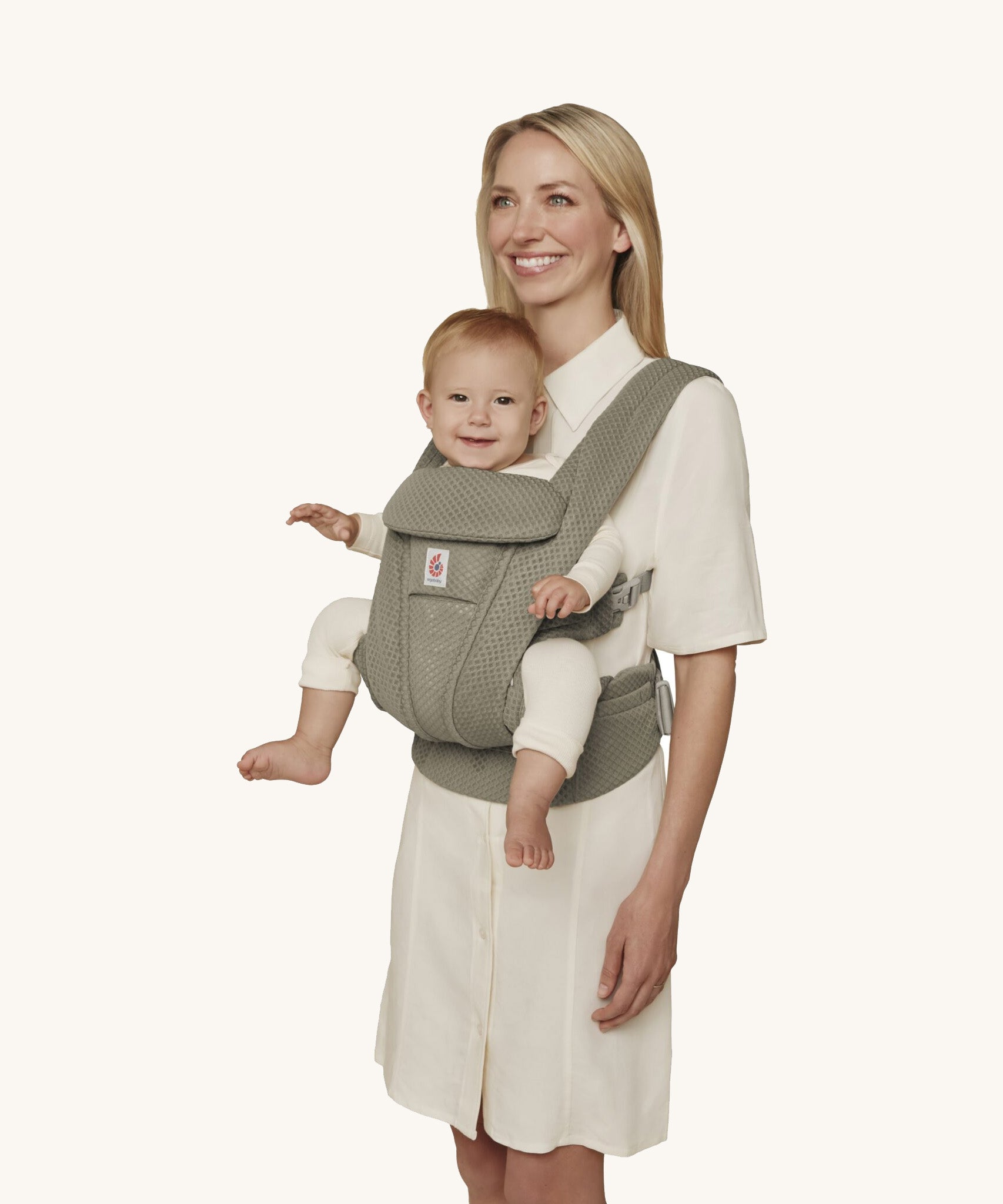 A woman wearing the Ergobaby Omni Deluxe Mesh baby carrier in Soft Olive, with a little baby being carried facing outwards. 