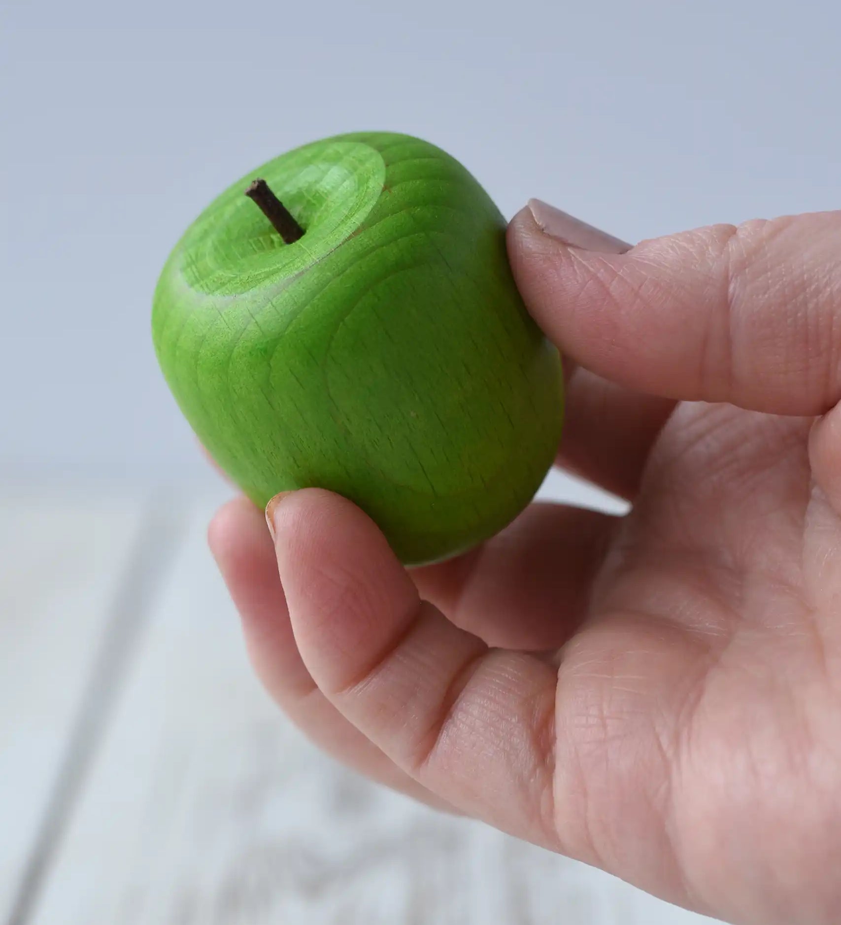 Erzi wooden green apple play food with a small green stem in an adult's hand.
