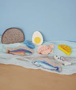 Pieces from the Erzi fish assortment wooden food play set placed on a blue coloured cloth in the Babipur playroom.