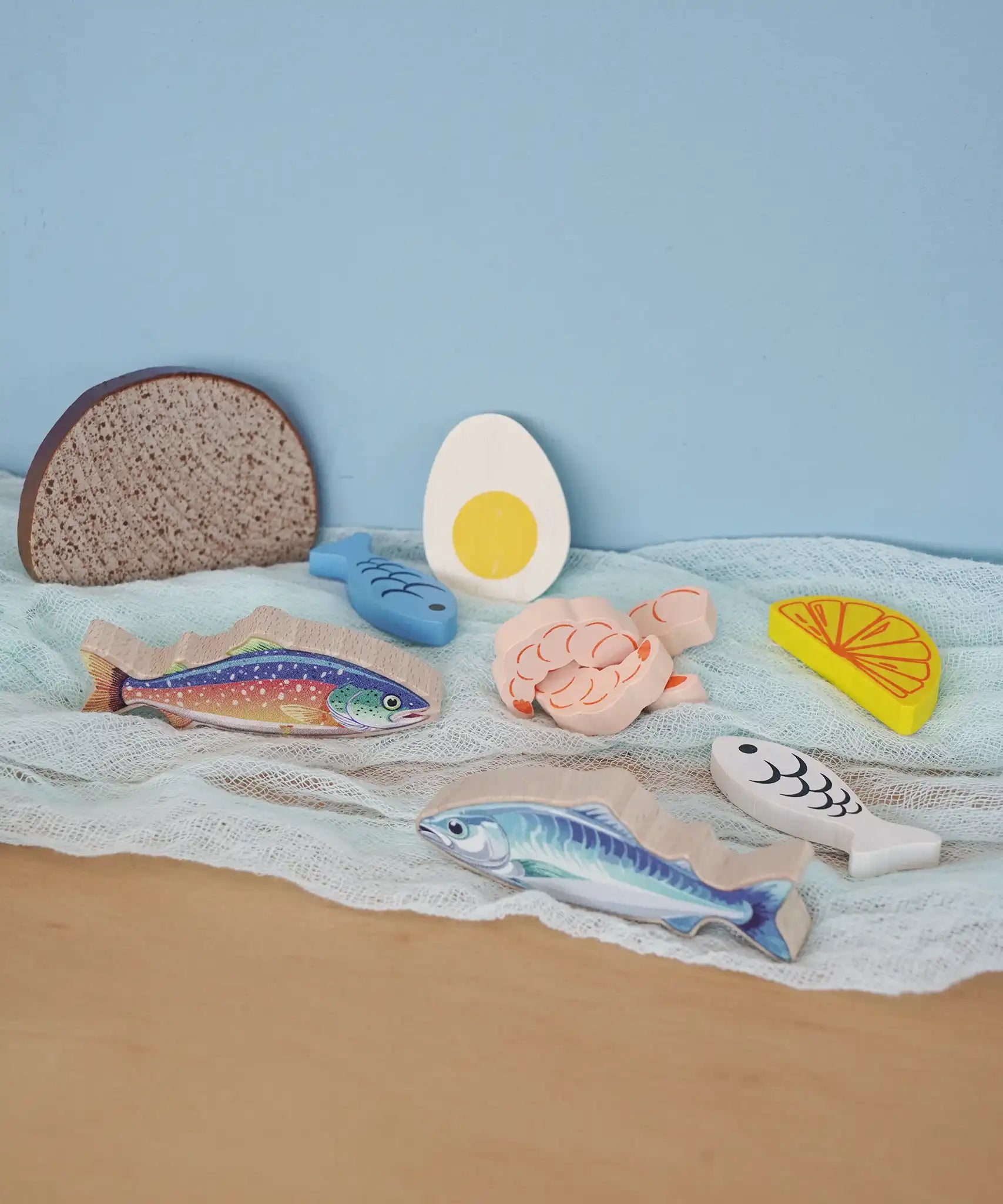 Pieces from the Erzi fish assortment wooden food play set placed on a blue coloured cloth in the Babipur playroom.