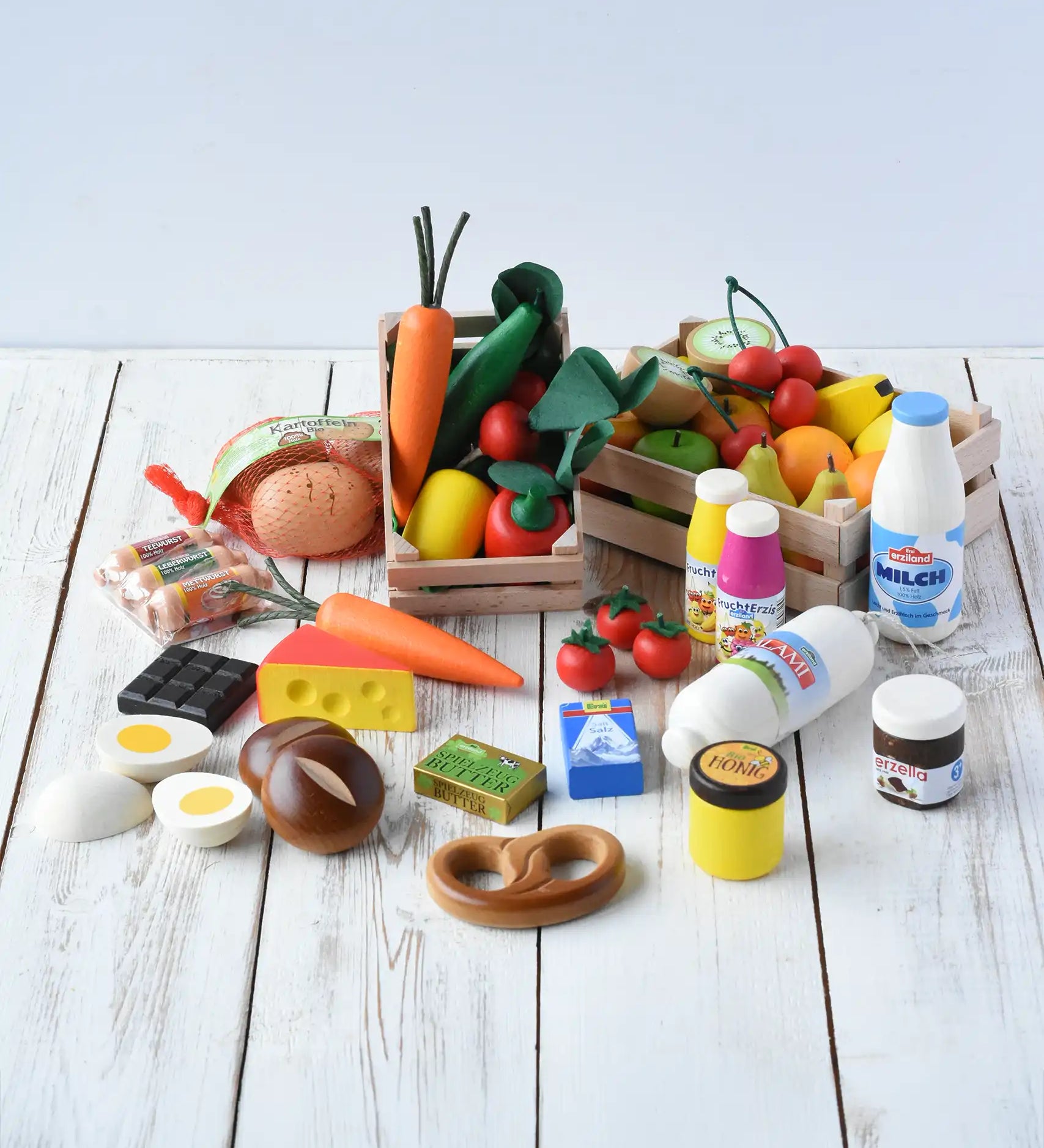 Erzi big shop assortment box wooden play food set placed on a wooden surface. A mix of vegetables, fruits, dairy products, drinks and packets and wooden crates. 