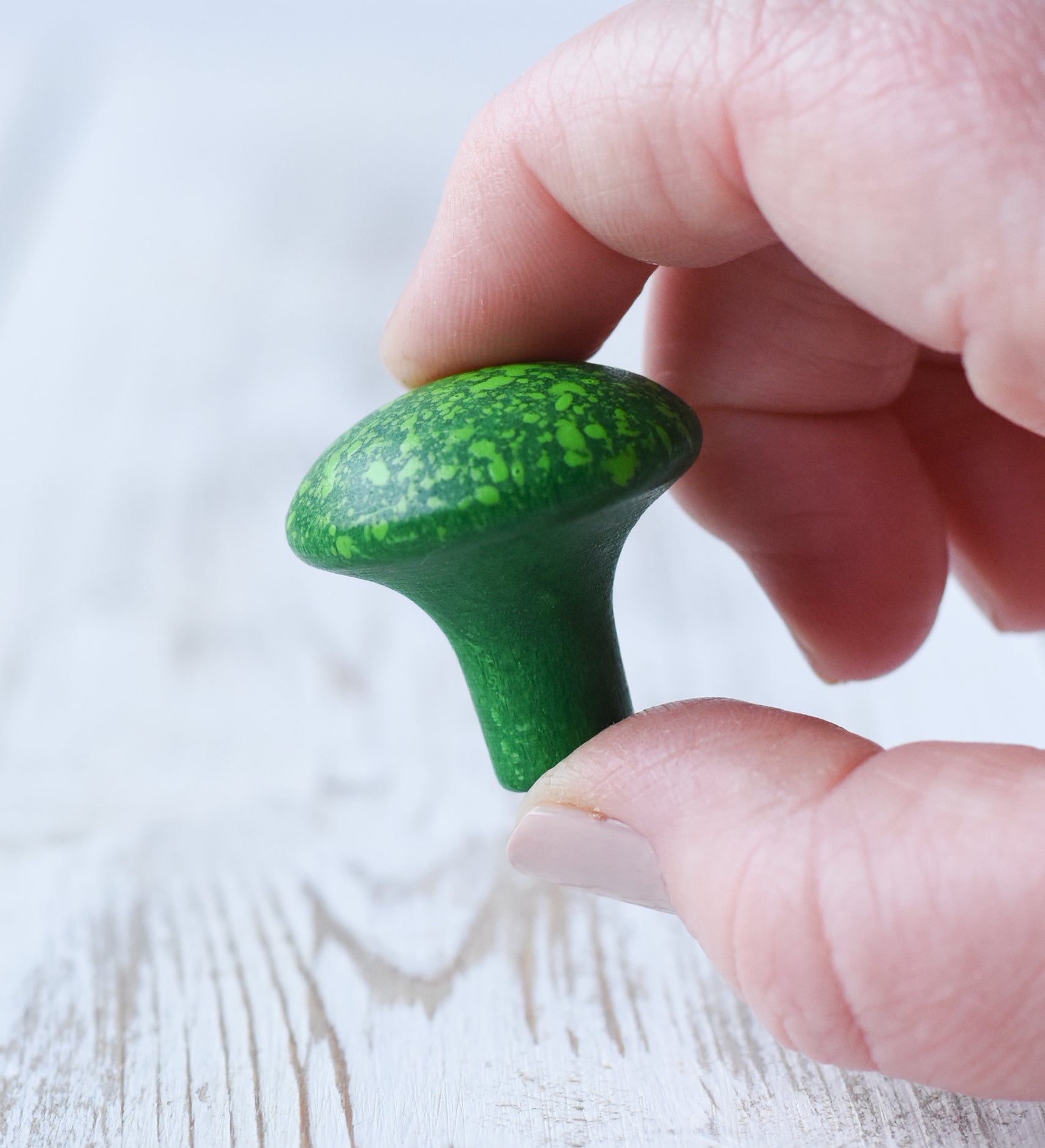 A close-up of a hand holding a small green floret of Erzi broccoli play food in an adult's hand.
