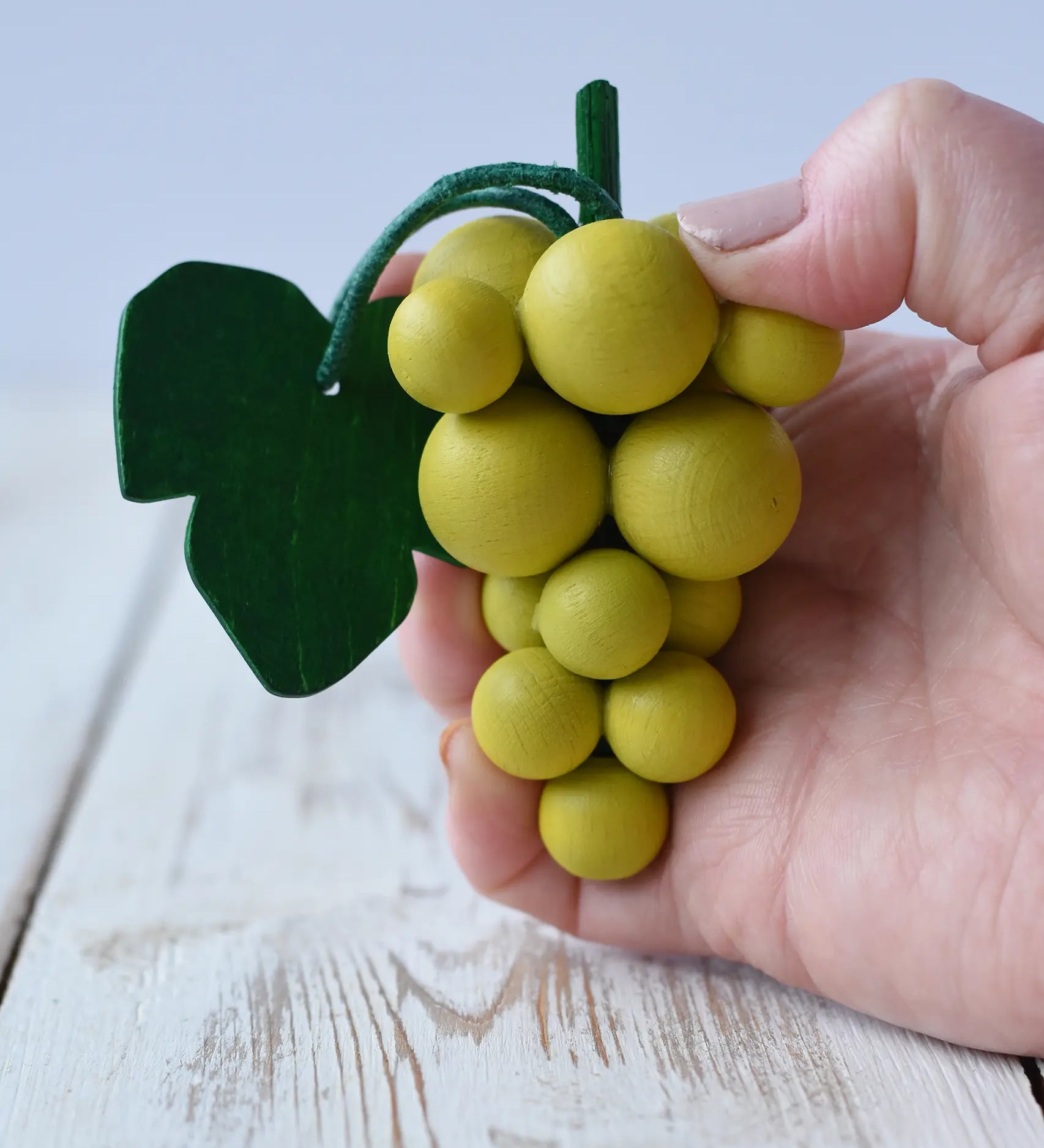 Erzi Bunch Of Green Grapes Wooden Play Food in an adult's hand.