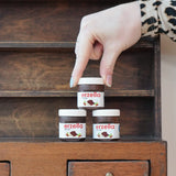 Three tubs of Erzi Erzella chocolate spread wooden play food stacked up with an adult's hand reaching for the one on top.