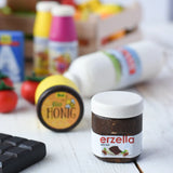 Erzi jar of Erzella hazelnut spread wooden play food placed on a wooden surface. Other Erzi toy play foods can be seen blurred in the background. 