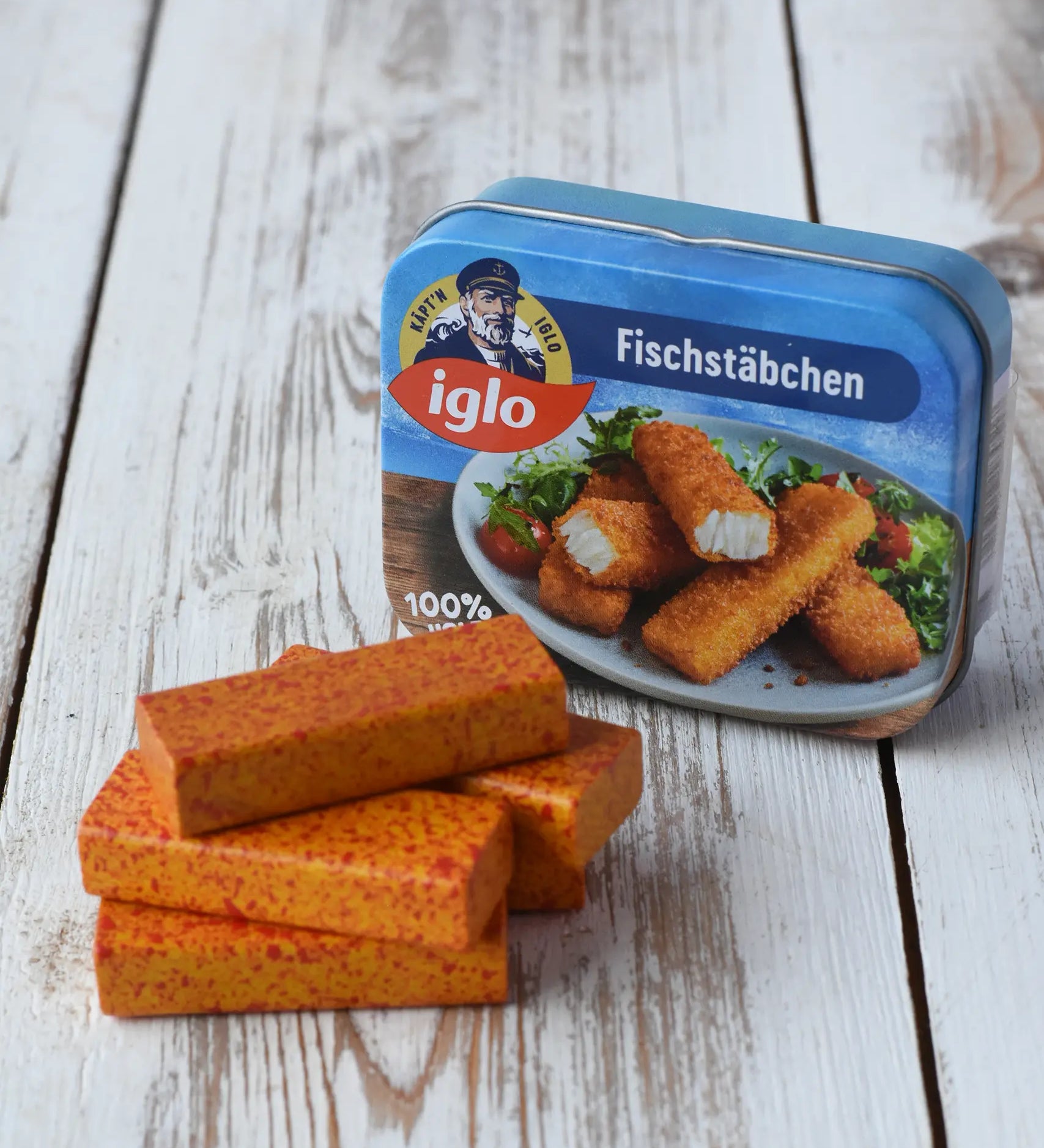 Erzi fish fingers in a tin wooden play food, wooden fish fingers placed on a wooden surface with the tin behind them. 