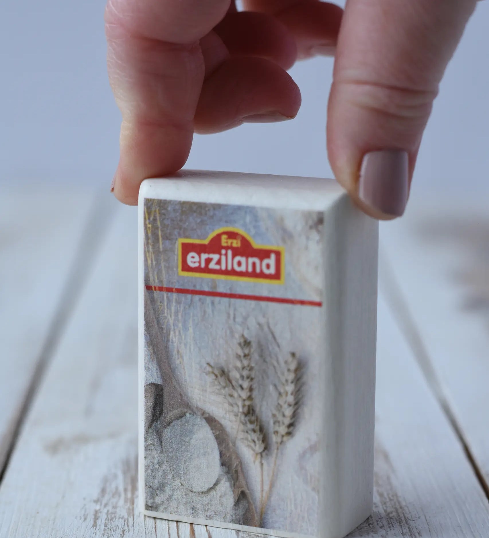 Erzi flour wooden play food placed on a wooden board with an adult's hand holding it.