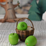 An Erzi green wooden toy apple placed in a Kraul basket. There are two other Erzi apples besides the basket.