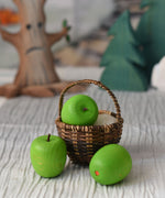 An Erzi green wooden toy apple placed in a Kraul basket. There are two other Erzi apples besides the basket.