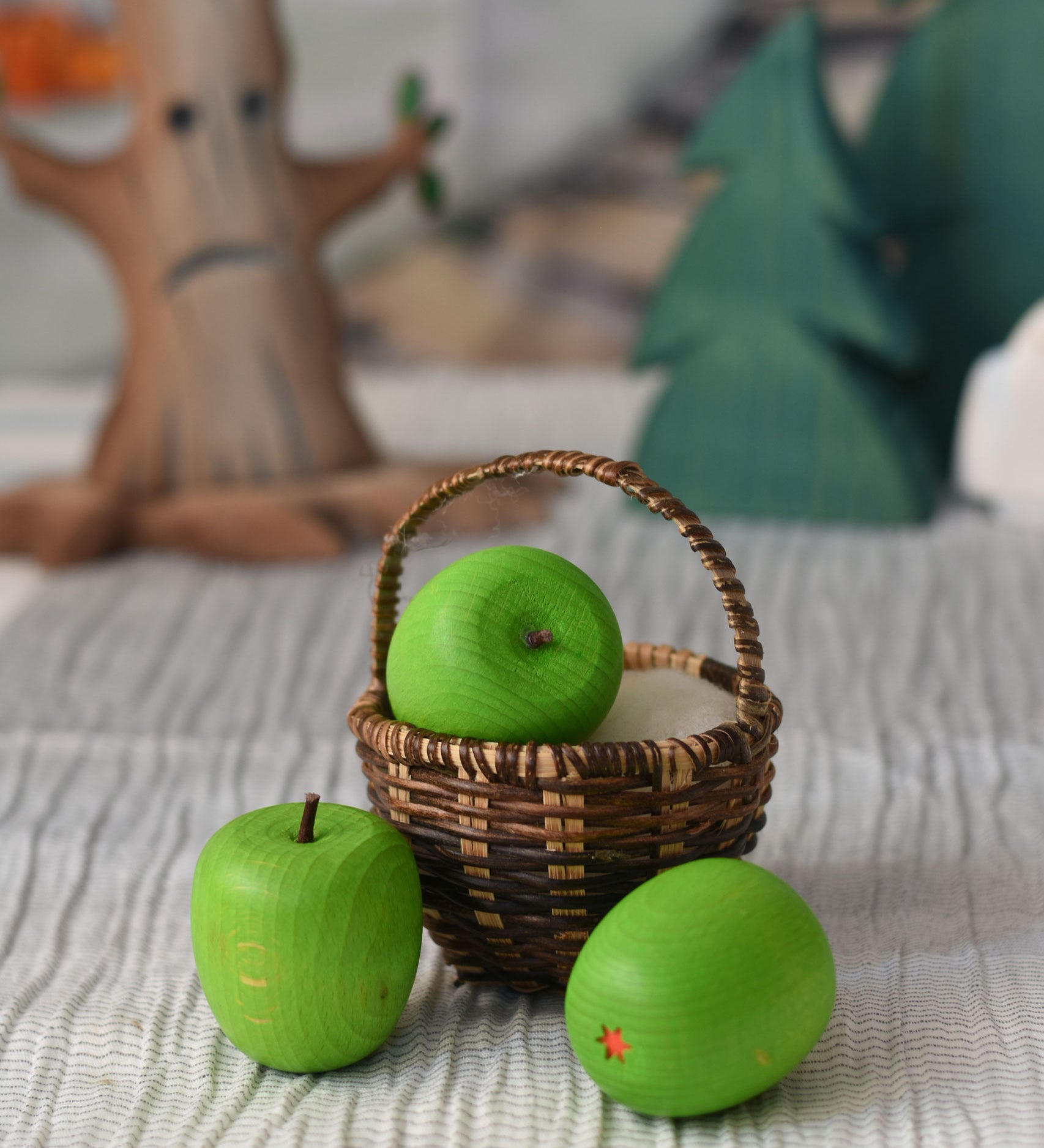 An Erzi green wooden toy apple placed in a Kraul basket. There are two other Erzi apples besides the basket.