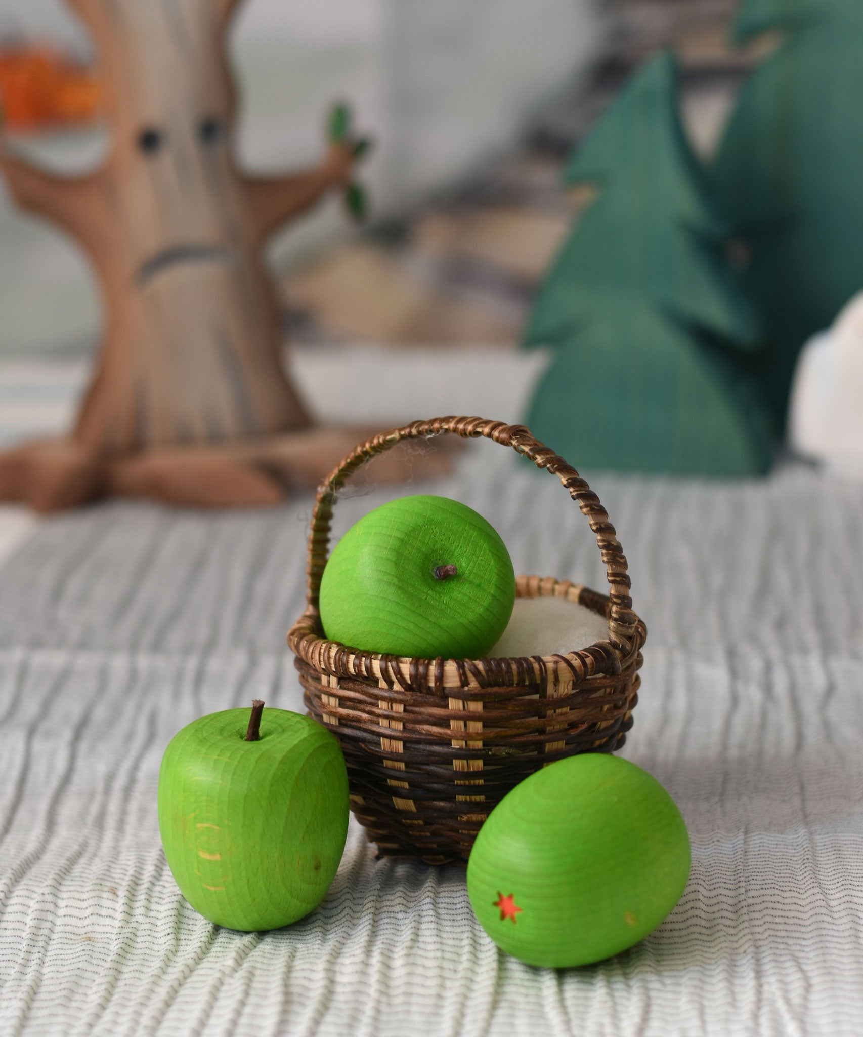 An Erzi green wooden toy apple placed in a Kraul basket. There are two other Erzi apples besides the basket.