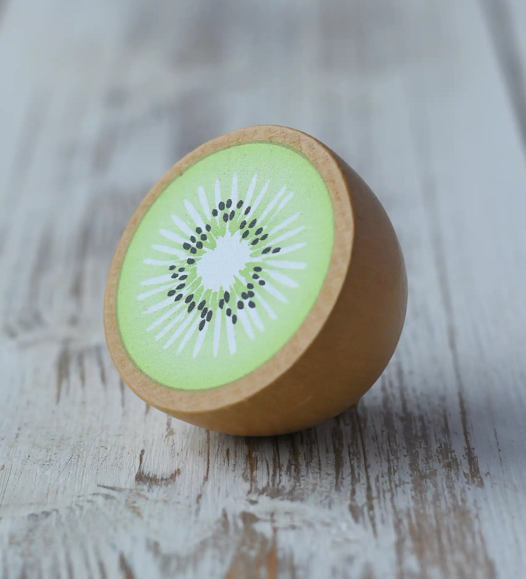 Erzi half kiwi fruit wooden play food placed on a wooden surface. 