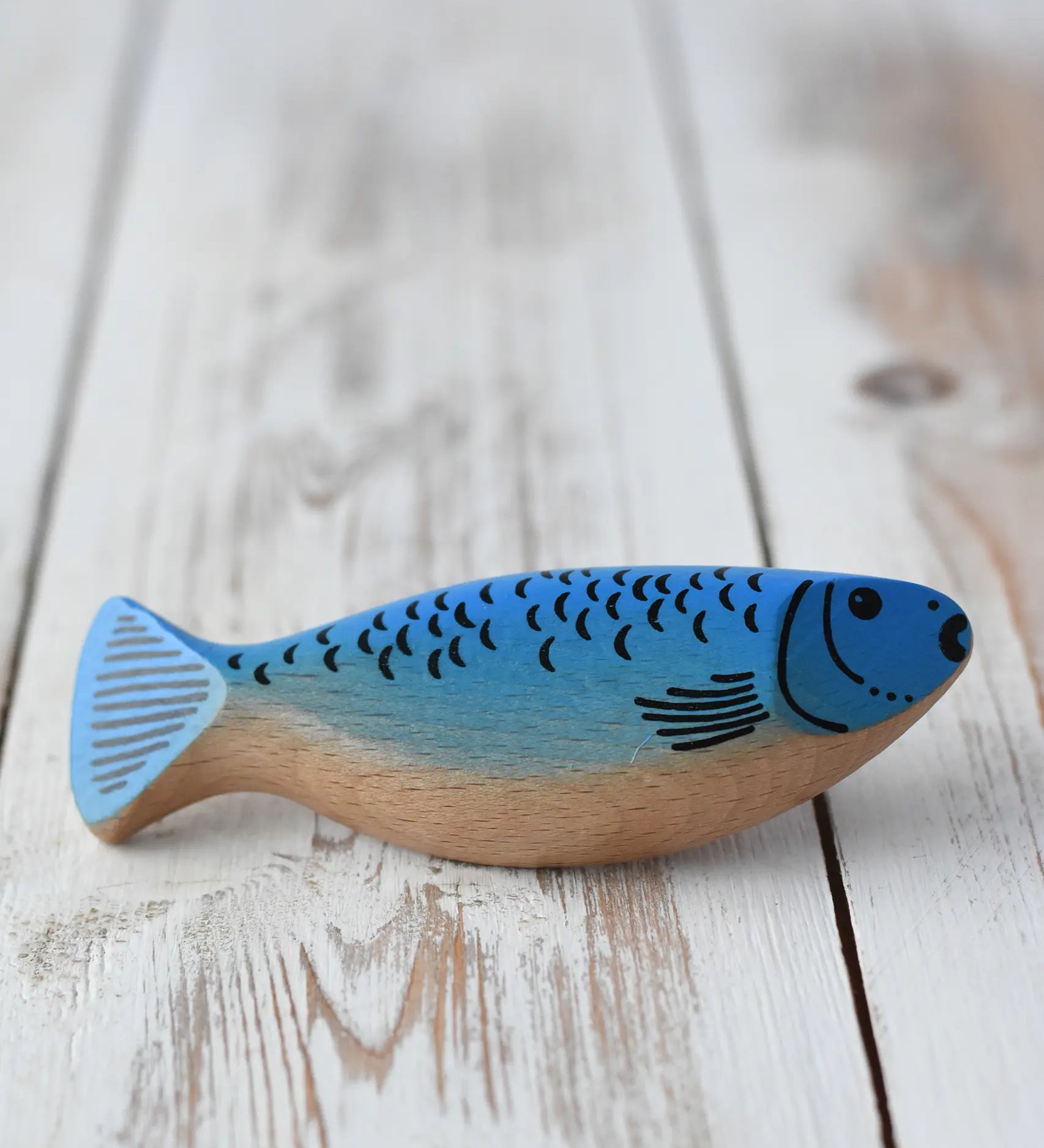 Erzi wooden toy herring fish with a blue painted top and a natural light wood belly, resting on a rustic white-washed wooden surface.