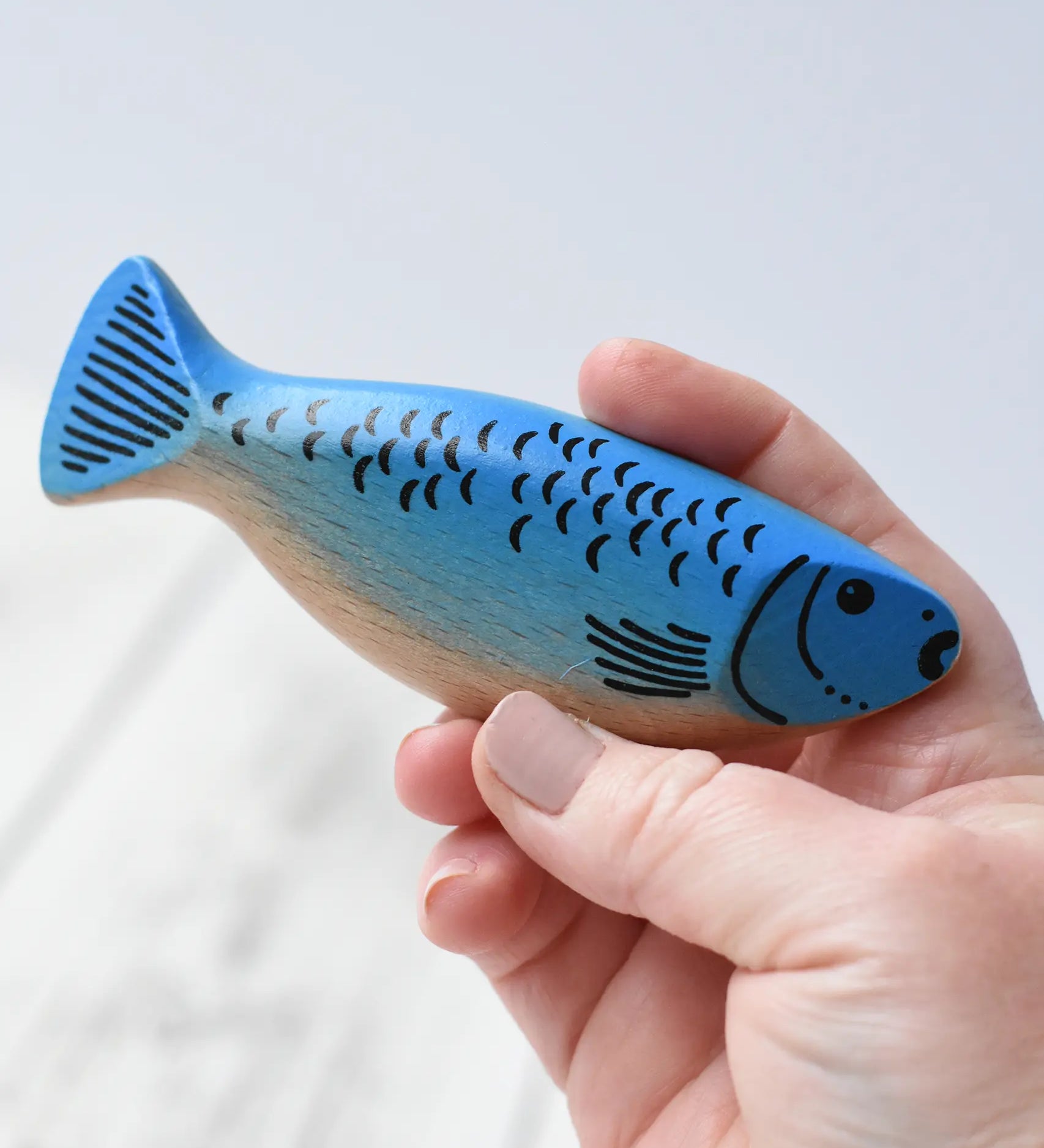 Erzi wooden toy herring fish with a blue painted top and a natural light wood belly in an adult's hand.