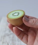 Erzi half kiwi fruit wooden play food in an adult's hand.