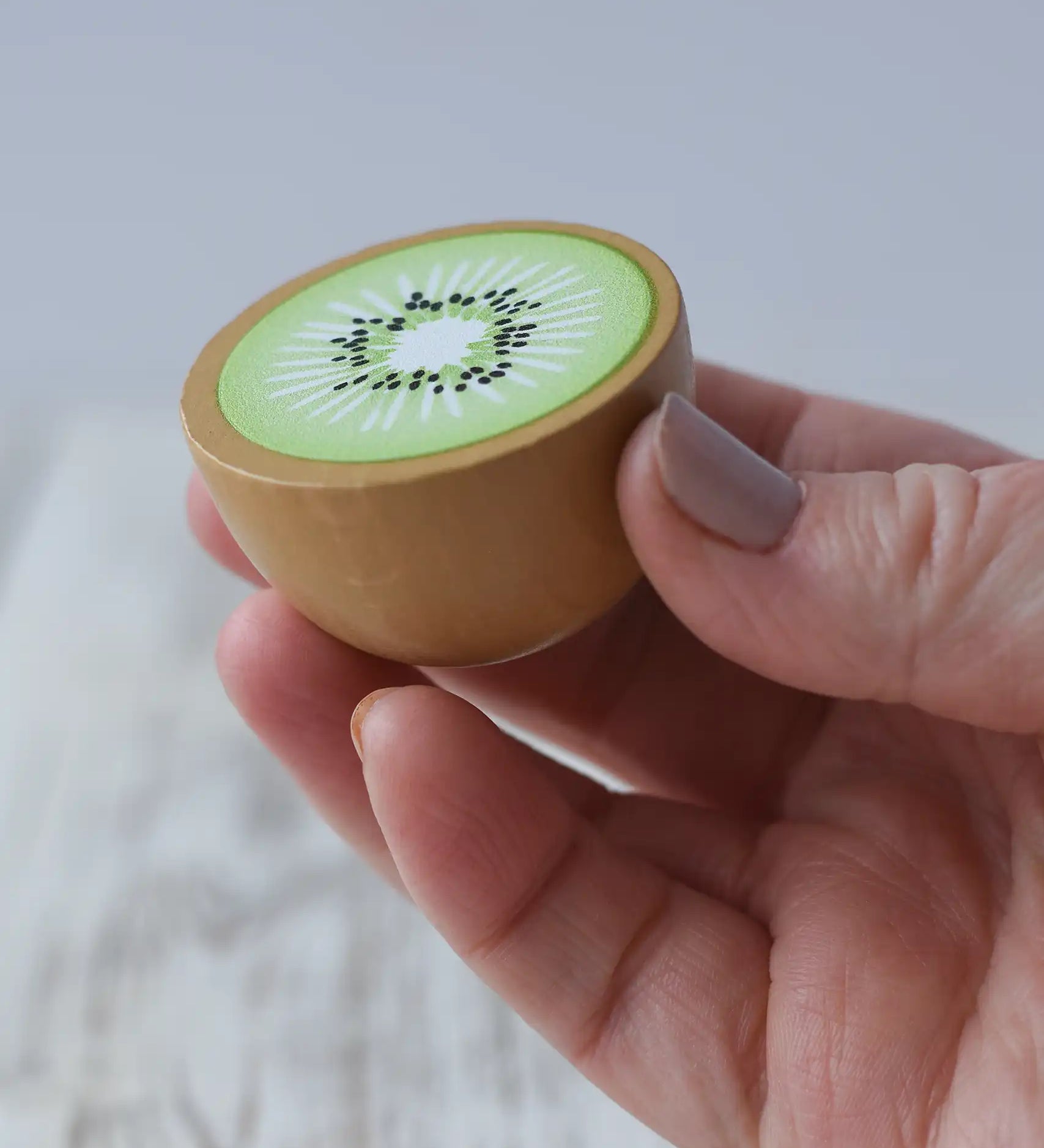 Erzi half kiwi fruit wooden play food in an adult's hand.