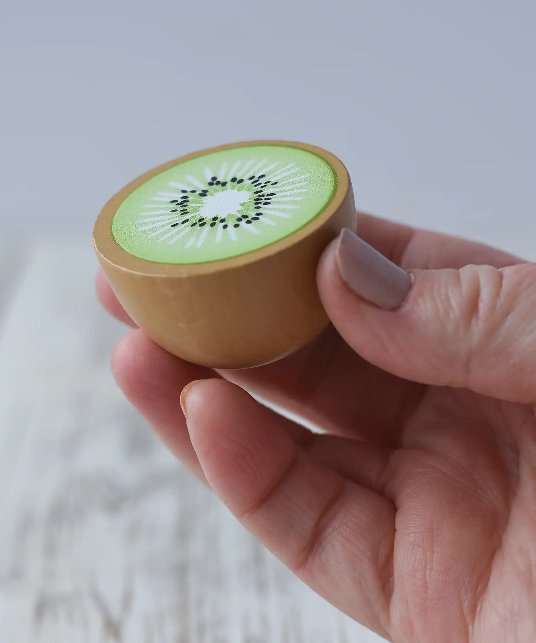 Erzi half kiwi fruit wooden play food in an adult's hand.