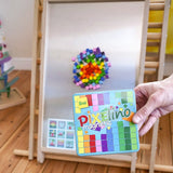 A hand holding a Erzi Pixelino tin with various coloured magnetic blocks on  a Triclimb Biri board in the Babipur playroom