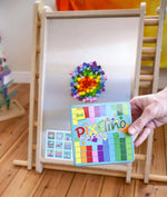 A hand holding a Erzi Pixelino tin with various coloured magnetic blocks on  a Triclimb Biri board in the Babipur playroom