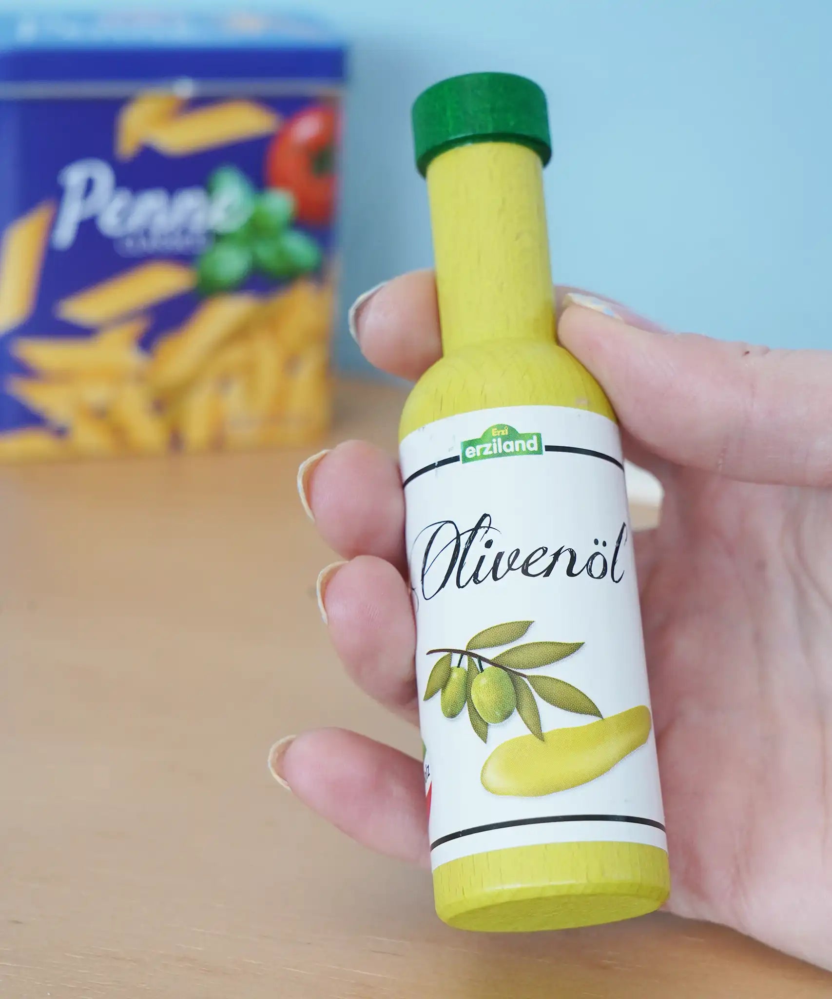 Erzi olive oil bottle wooden play food in an adult's hand in the Babipur playroom.