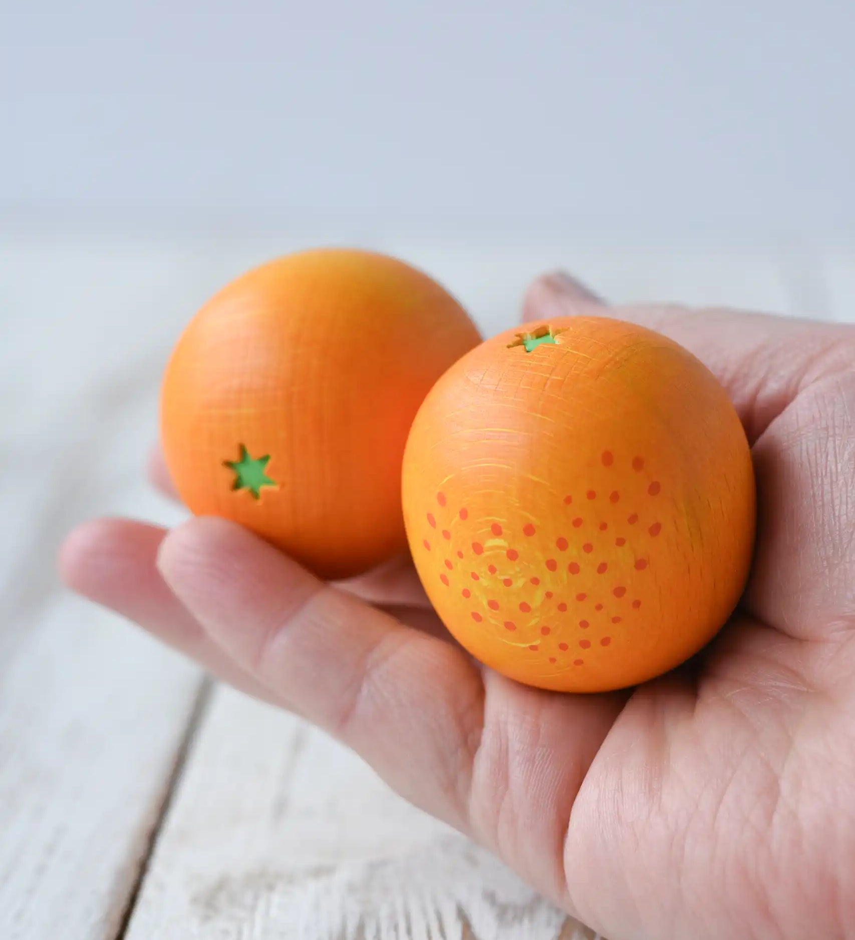 Two Erzi orange wooden play food toys in an adult's hand.