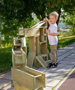 Child playing with the Erzi wooden outdoor building block set. The blocks have been set up to form a ball run.