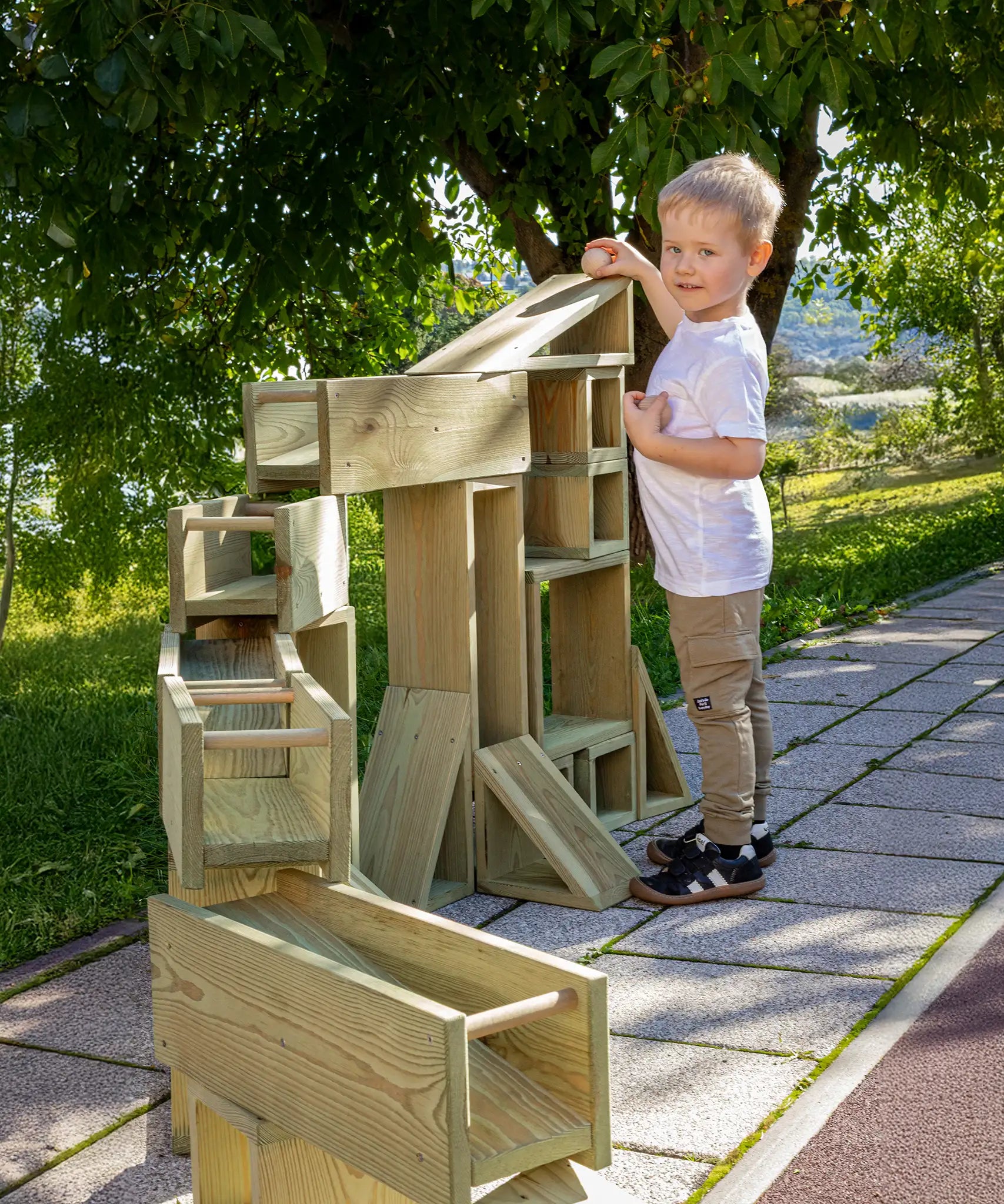 Child playing with the Erzi wooden outdoor building block set. The blocks have been set up to form a ball run.
