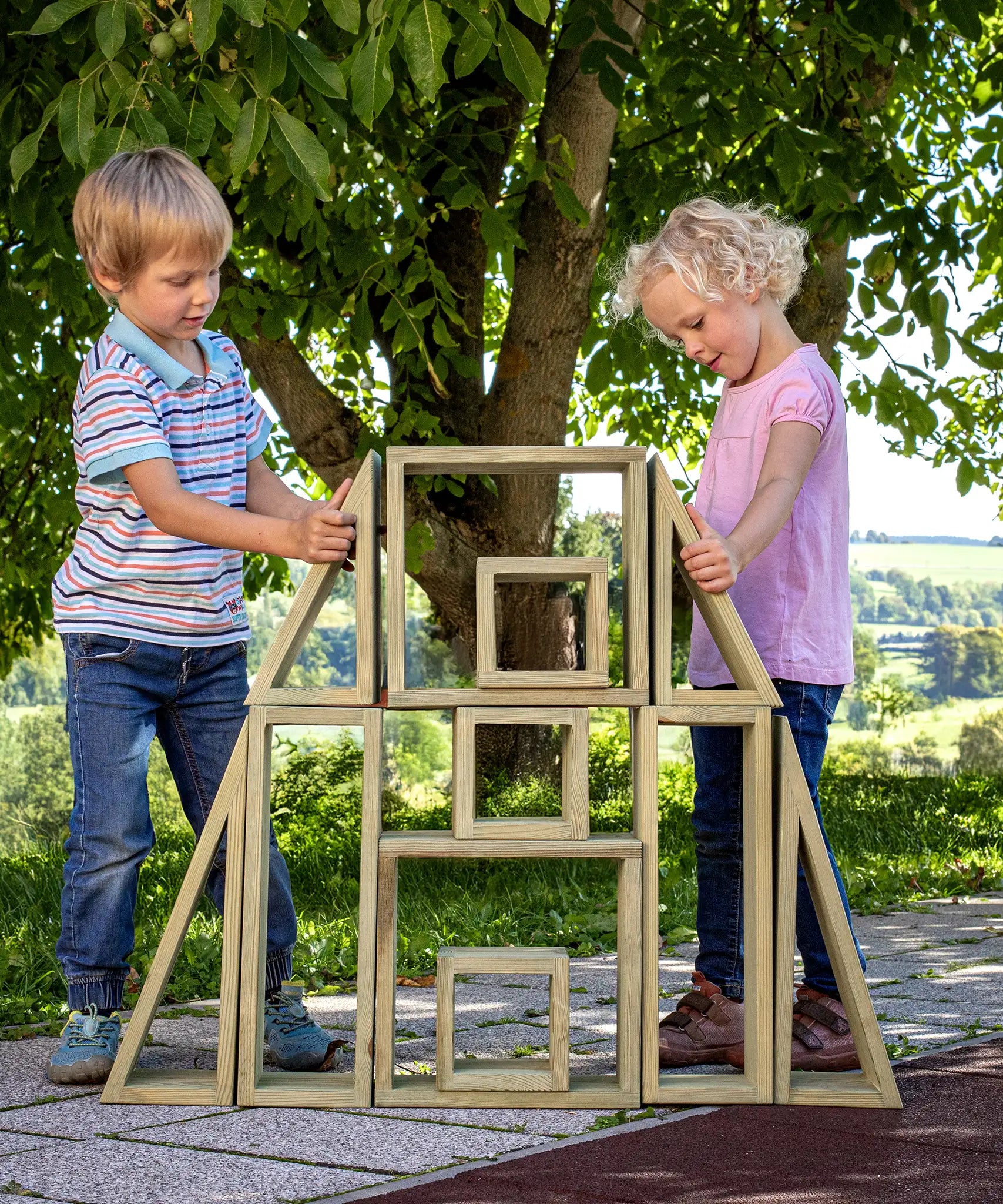 Children playing with the Erzi wooden outdoor building block set. They are stacking the large blocks on top of each other.