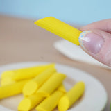 Adult hand holding a loose Erzi penne pasta piece showing scale