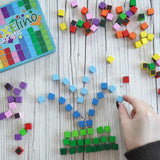 A hand making a fountain using colorful small Erzi magnetic blocks from the pixelino set next to a branded tin