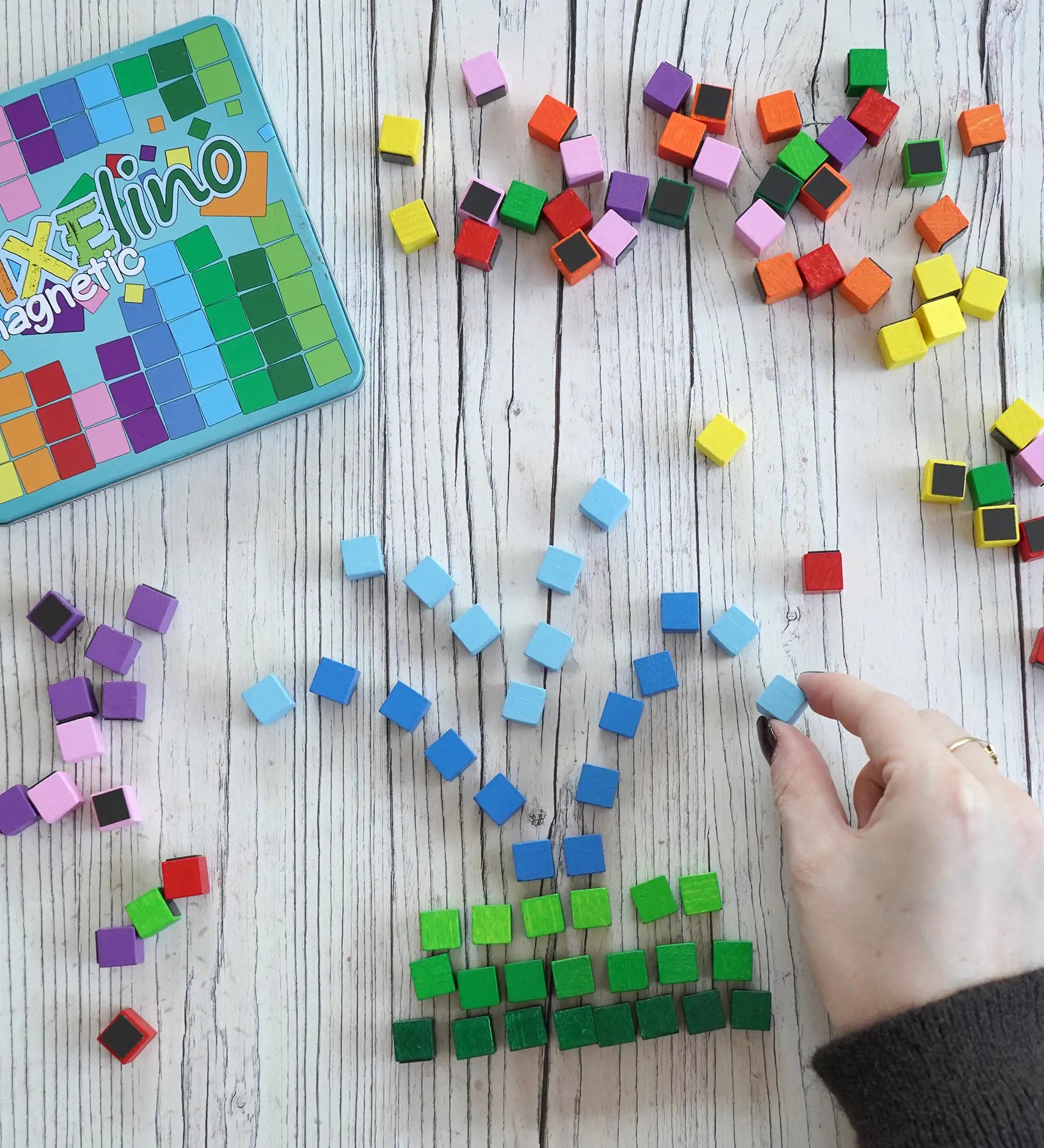A hand making a fountain using colorful small Erzi magnetic blocks from the pixelino set next to a branded tin