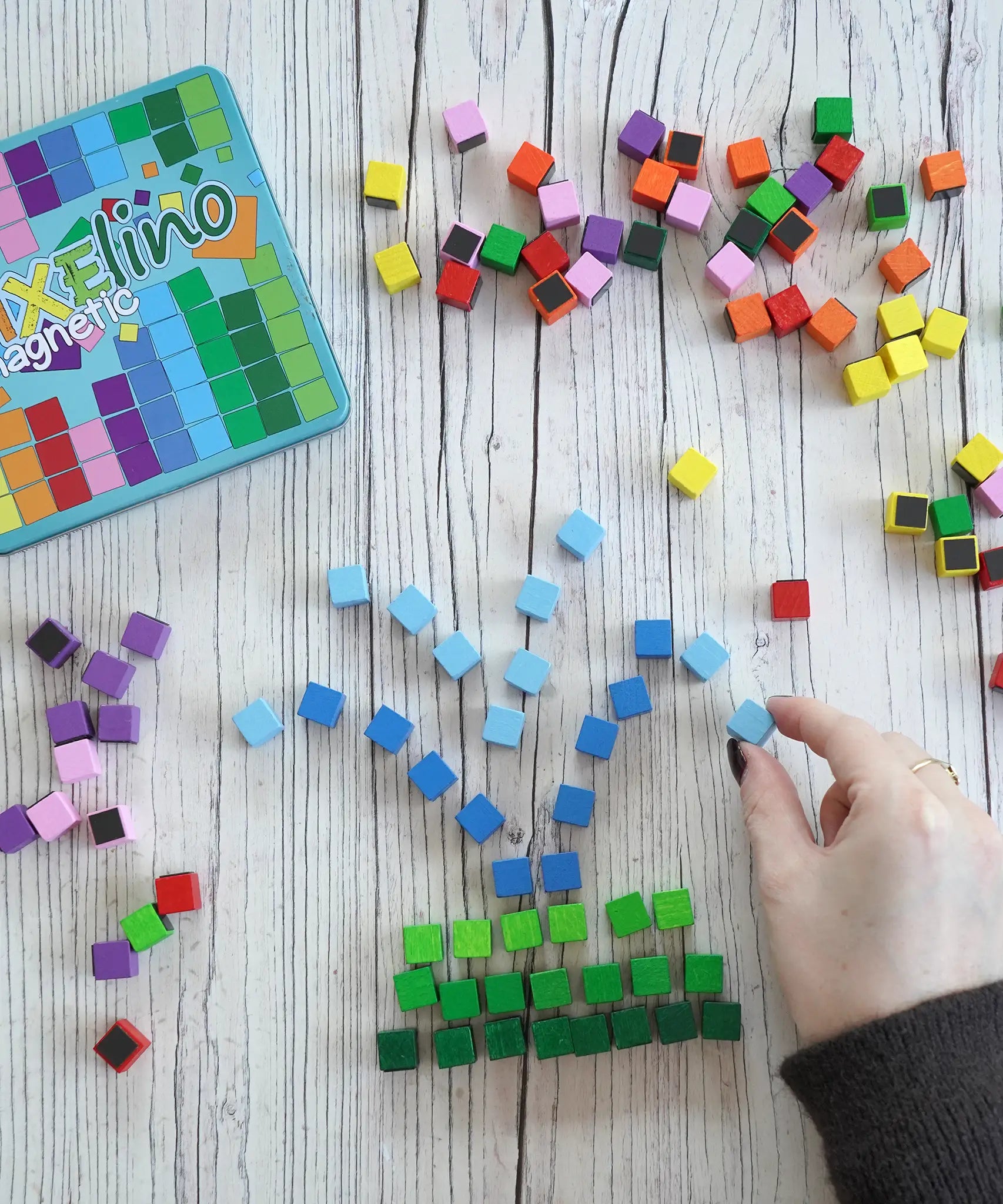 A hand making a fountain using colorful small Erzi magnetic blocks from the pixelino set next to a branded tin