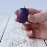 Erzi Plum Wooden Play Food in an adult's hand. Purple plum with a small green stock.