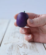 Erzi Plum Wooden Play Food in an adult's hand. Purple plum with a small green stock.