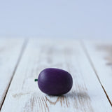 Erzi Plum Wooden Play Food placed on a wooden board. Purple plum with a small green stock.