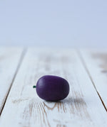 Erzi Plum Wooden Play Food placed on a wooden board. Purple plum with a small green stock.