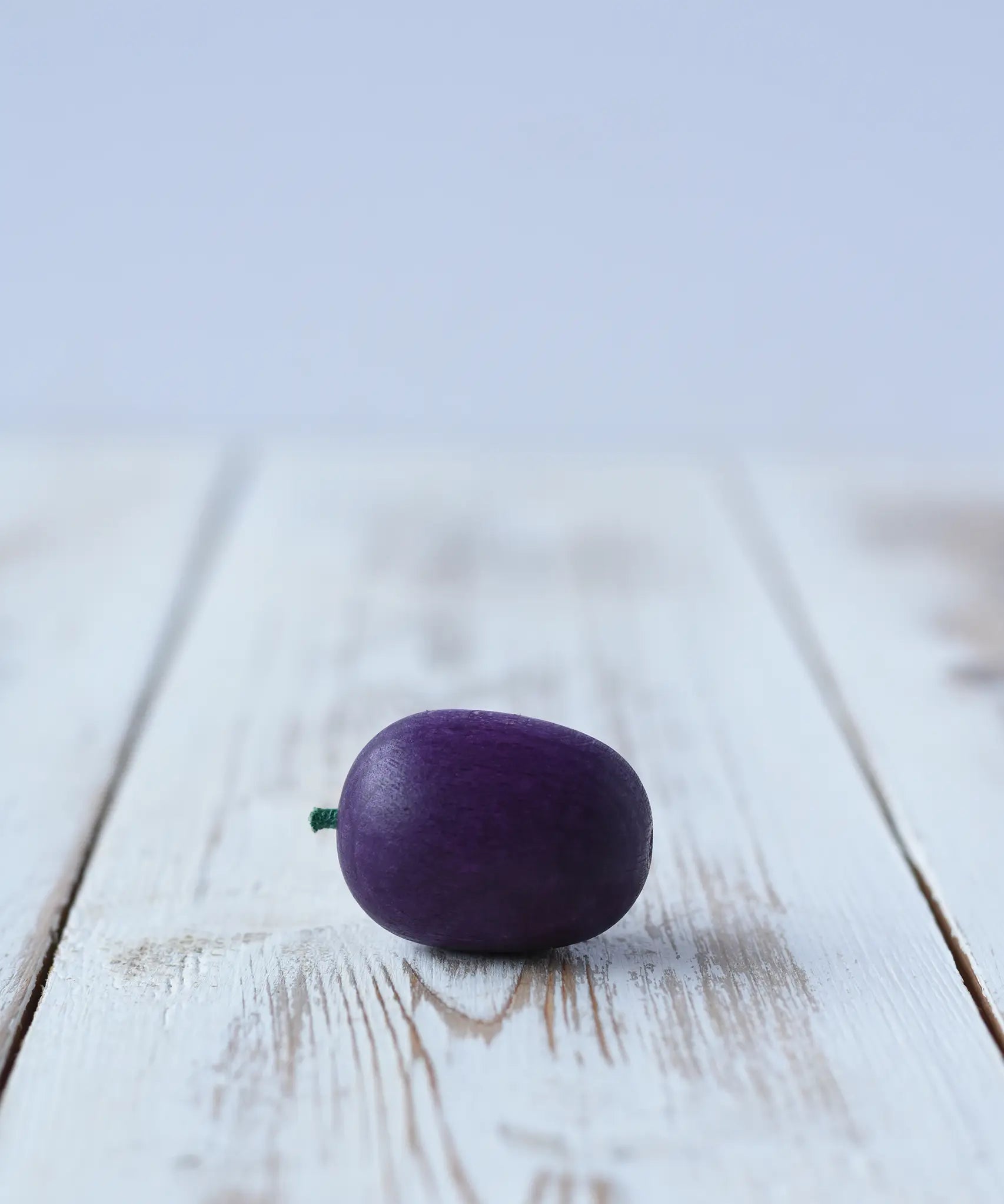 Erzi Plum Wooden Play Food placed on a wooden board. Purple plum with a small green stock.