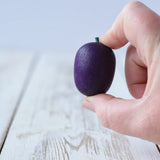 Erzi Plum Wooden Play Food in an adult's hand. Purple plum with a small green stock.