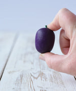 Erzi Plum Wooden Play Food in an adult's hand. Purple plum with a small green stock.