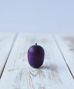 Erzi Plum Wooden Play Food placed on a wooden board. Purple plum with a small green stock.