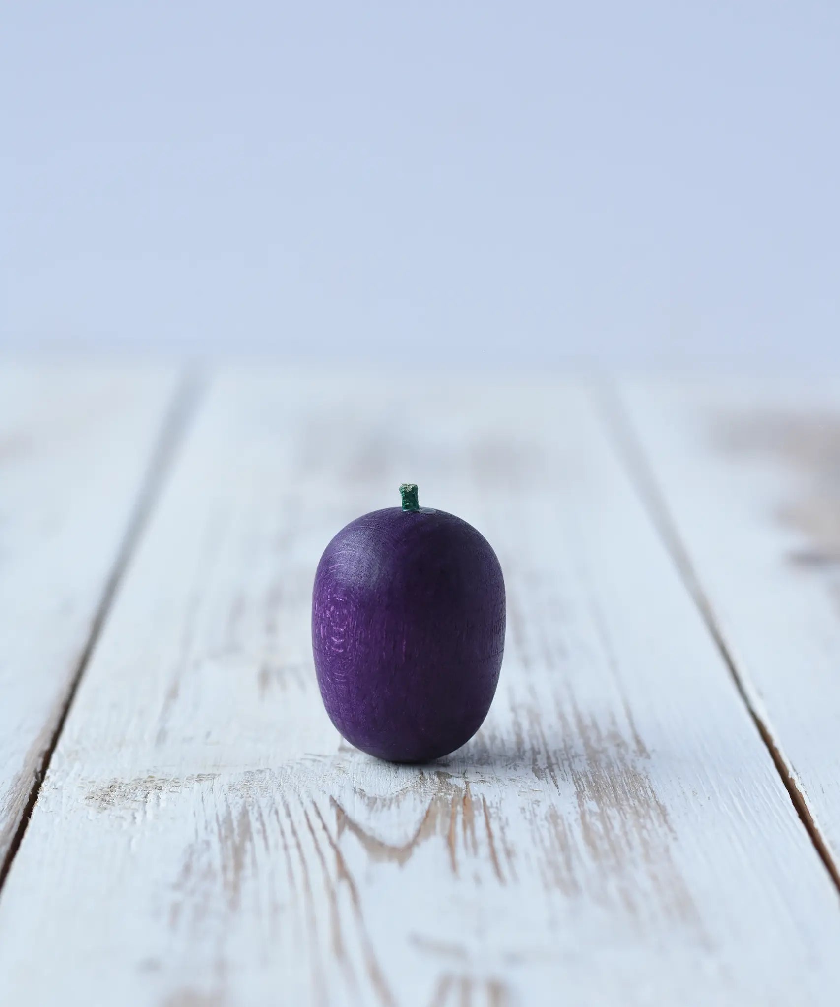 Erzi Plum Wooden Play Food placed on a wooden board. Purple plum with a small green stock.