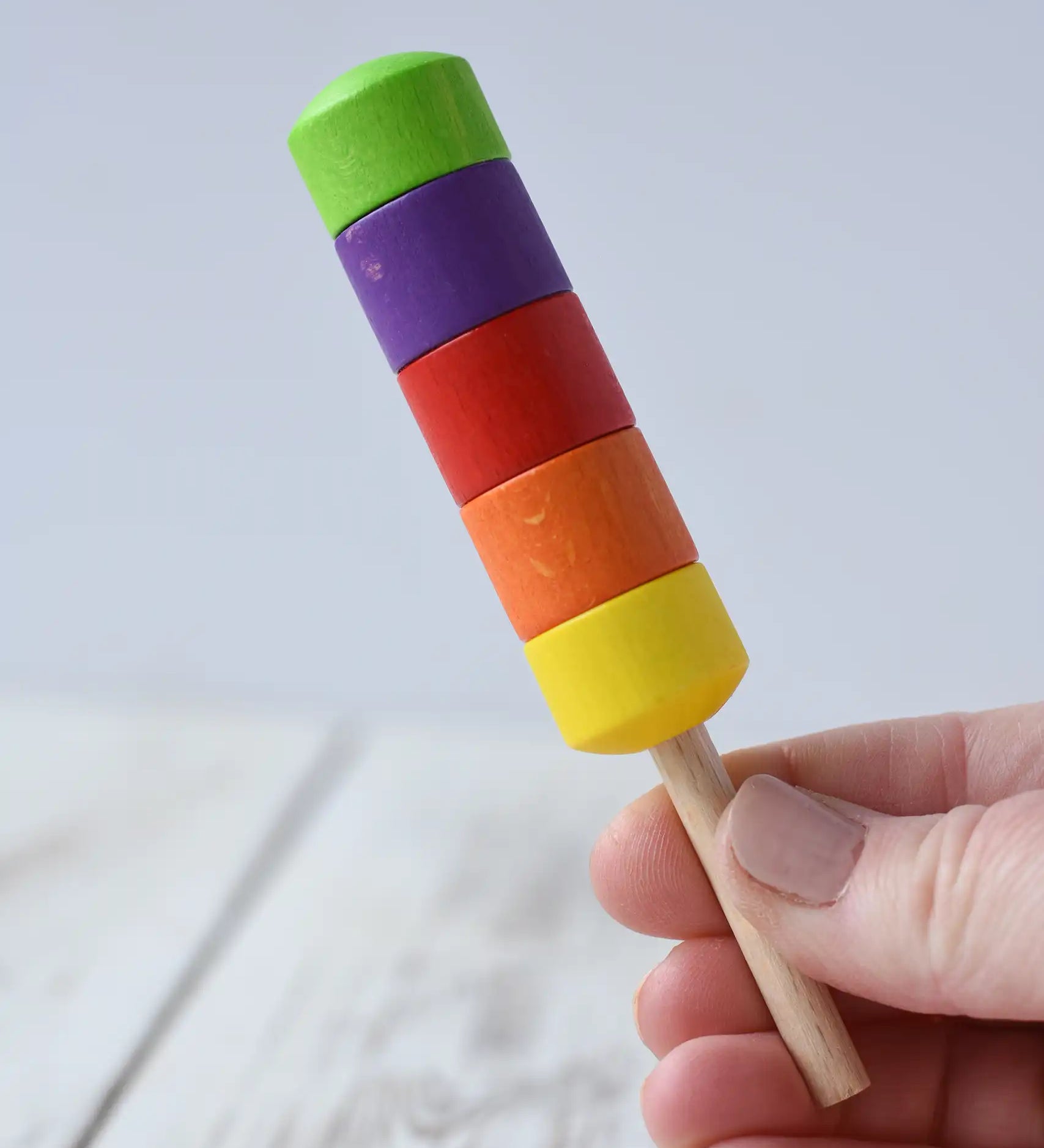 Erzi rainbow ice lolly wooden play food in an adult's hand.