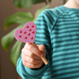Erzi pink raspberry heart shaped ice lolly wooden play food in a child's hand.
