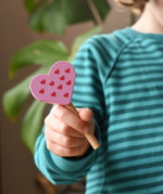 Erzi pink raspberry heart shaped ice lolly wooden play food in a child's hand.
