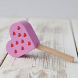 Erzi pink raspberry heart shaped ice lolly wooden play food placed on a wooden surface.
