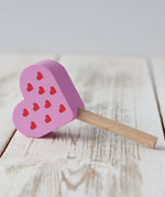 Erzi pink raspberry heart shaped ice lolly wooden play food placed on a wooden surface.
