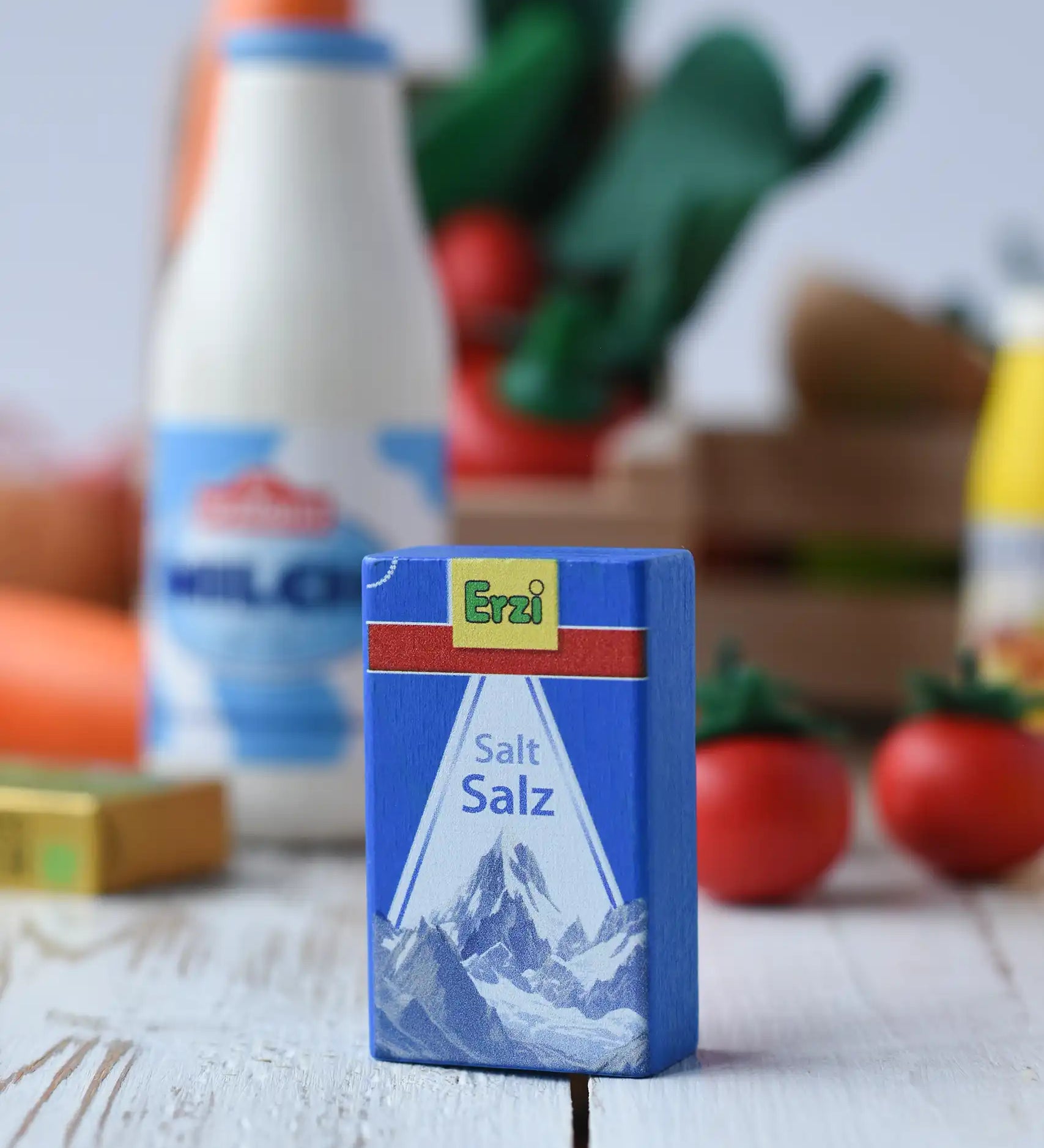 Erzi salt wooden play food packet placed on a wooden surface. Blue packet with erzi branding on the front. Other Erzi play food toys can be seen in the backgroud.