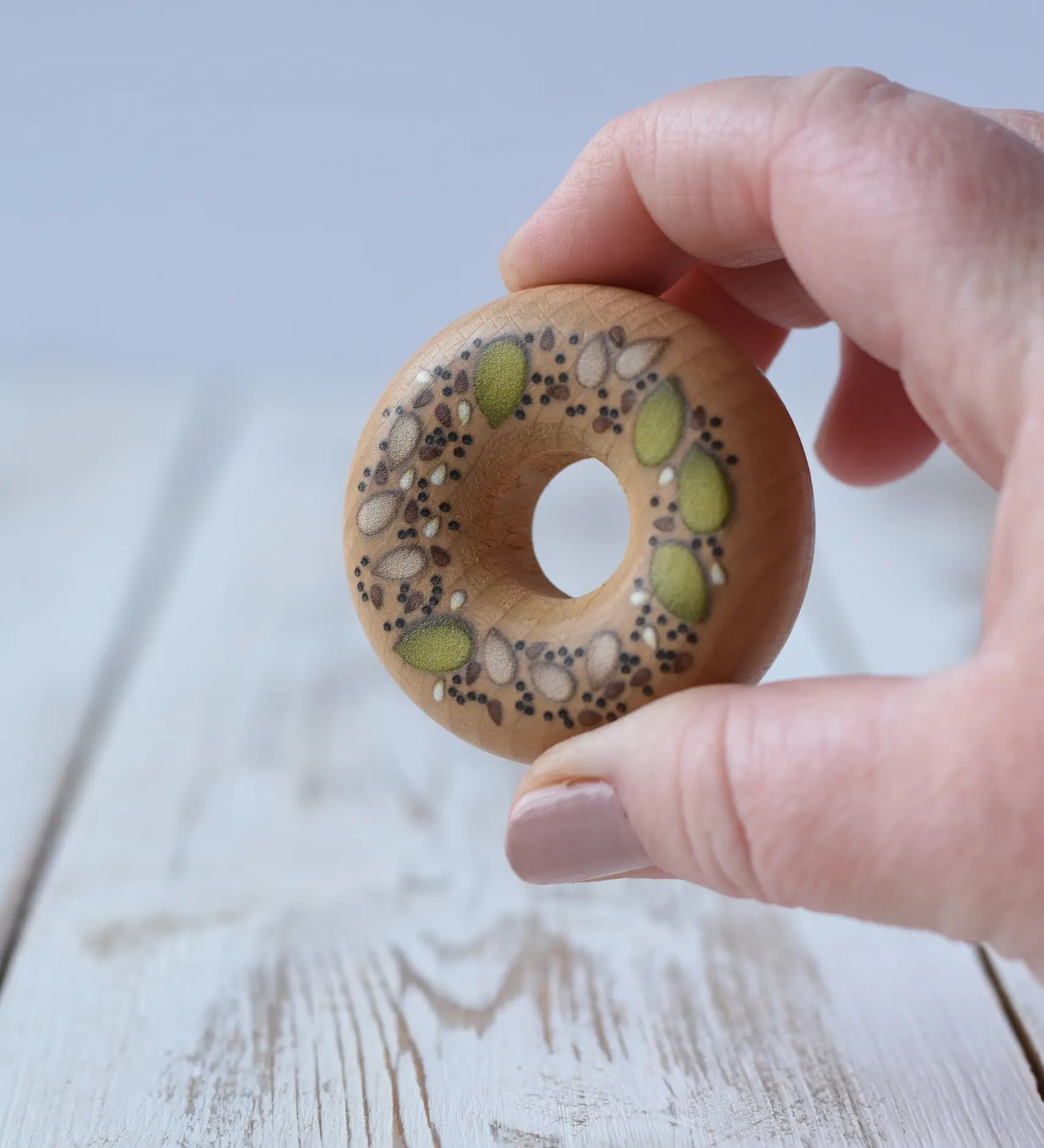 Erzi seeded bagel wooden play food in an adult's hand.