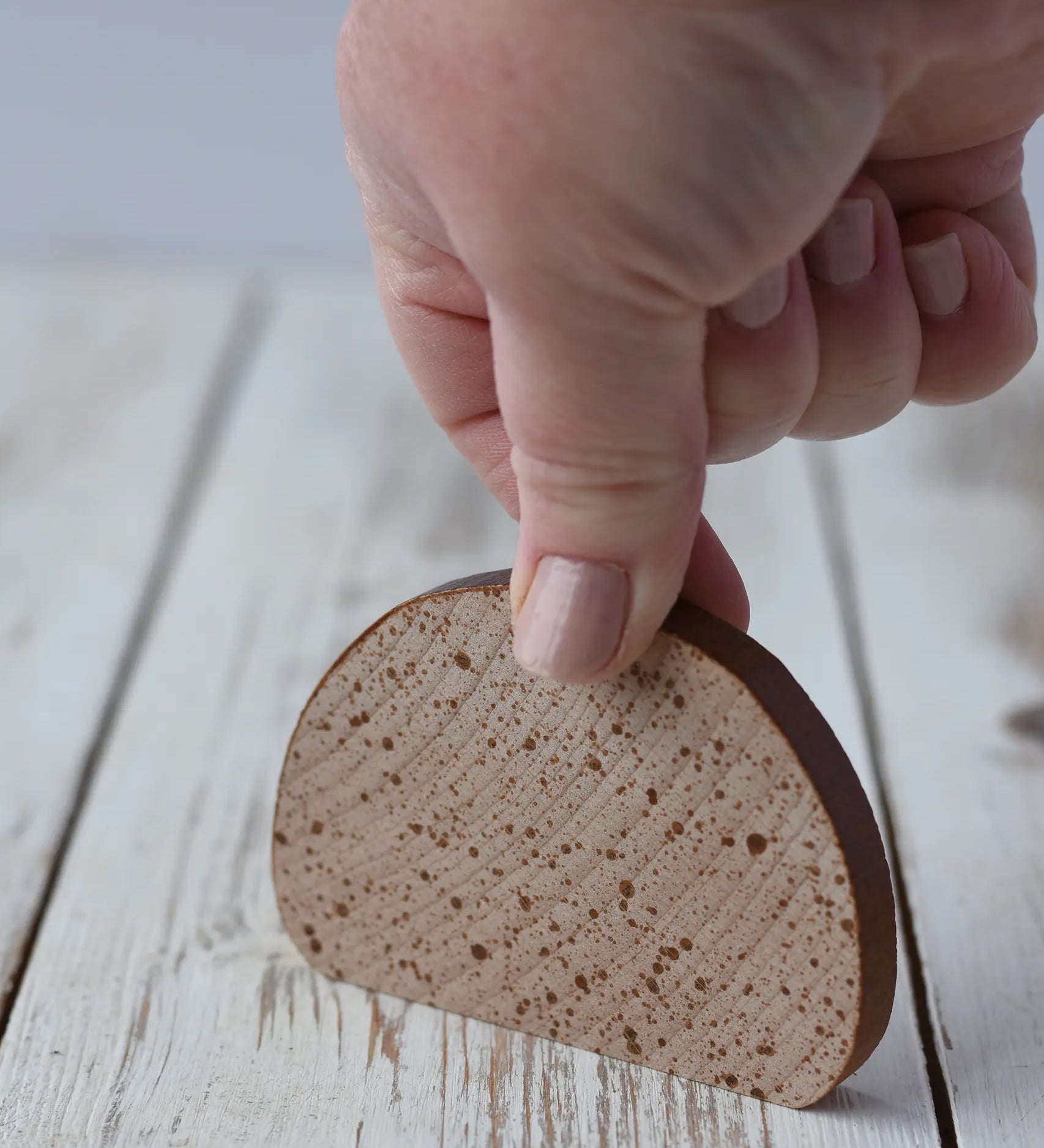 A hand holding an Erzi wooden slice of Bread play food placing it onto a wooden surface.